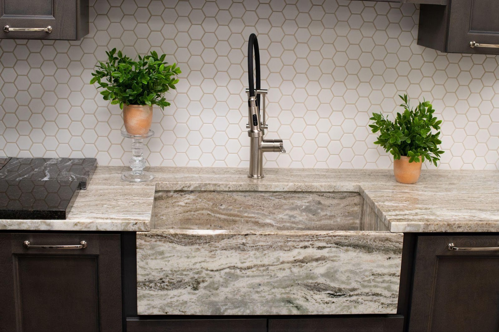 A kitchen sink with a marble counter top and a plant.